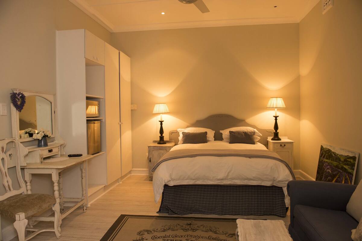 A bedroom with a bed, bedside lamps, a dresser, a chair, and a painting on the wall.