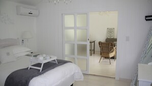 A bedroom with a bed, bedside table, and a tray with tea set. There is a door leading to a dining area with a chair and a table. - Lemon Tree B&B (Kloof)