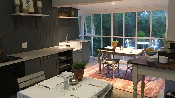 A modern kitchen with a large window, a dining area with a table and chairs, and a built-in oven. - Lemon Tree B&B (Kloof)