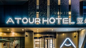 Entrada de hotel moderna con señalización iluminada, puerta de acceso de vidrio y un área de descanso al aire libre.