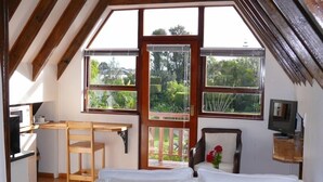 A bedroom with a bed, a wooden desk, and a chair. There are large windows with a view of greenery outside. - Aberdour Guesthouse (Gqeberha (Port Elizabeth))