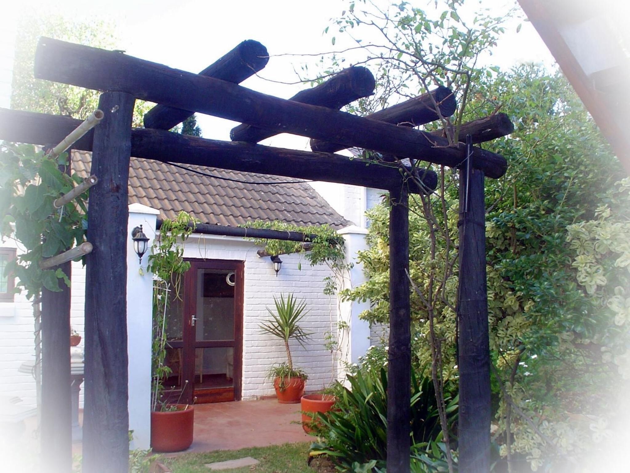 A small house with a tiled roof, a wooden pergola, and potted plants.