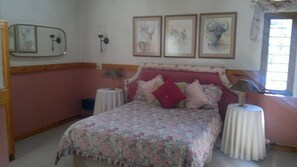 A bedroom with a floral bedspread, a pink headboard, and three framed pictures on the wall.