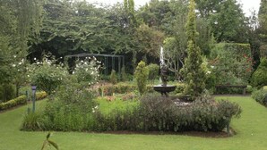 A lush garden with a central fountain, surrounded by various plants and a pergola structure. - Highland Rose Country House & Serenity Spa (Dullstroom)