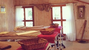 A room with wooden walls and a sloped ceiling, featuring a long table with red cloths and baskets, a chair, and a window with curtains. - Highland Rose Country House & Serenity Spa (Dullstroom)