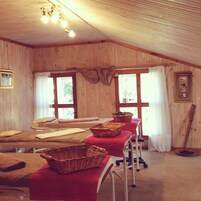 Una habitación con paredes de madera y techo inclinado, que presenta una mesa larga con manteles rojos y cestas, una silla y una ventana con cortinas.