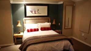 A neatly made bed with a striped blanket, a framed artwork above it, and a bedside lamp on each side. - Highland Rose Country House & Serenity Spa (Dullstroom)