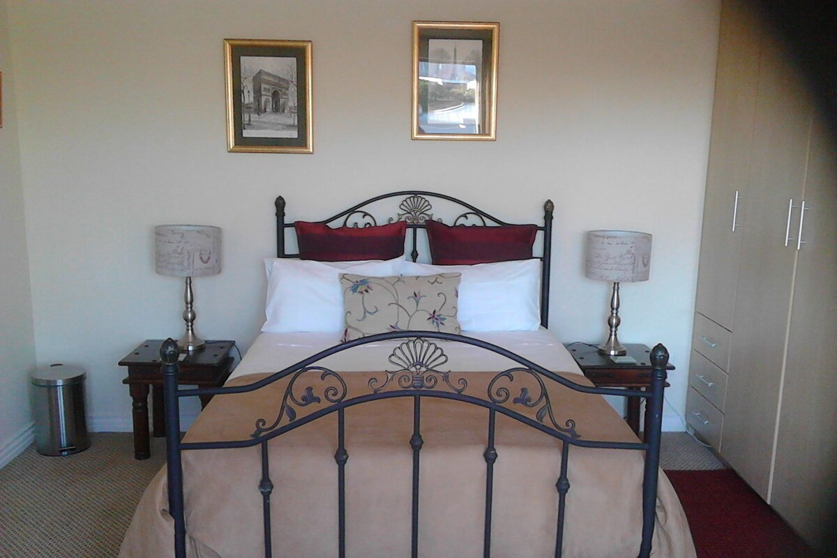 A bed with a metal frame, two bedside tables, two lamps, a red carpet, and two framed pictures on the wall.