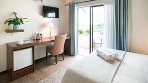 A hotel room with a bed, a desk with a chair, a TV, a plant, and a view of the outdoors. - Sandton Slippers (Sandton)