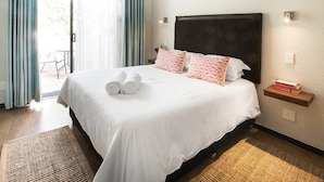 A neatly made bed with white linens and pink patterned pillows, a wooden headboard, and a small bedside table with books. - Sandton Slippers (Sandton)