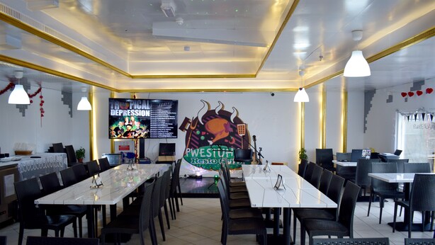 A restaurant with multiple tables and chairs, a large menu board, and a television screen displaying a menu. - Kings Park Hotel (Dubai)
