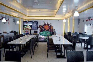 A restaurant with multiple tables and chairs, a large menu board, and a television screen displaying a menu. - Kings Park Hotel (Dubai)