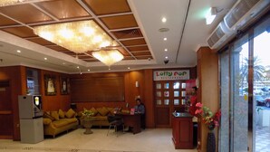 A lobby with a reception desk, a sofa, a refrigerator, and a chandelier. - Kings Park Hotel (Dubai)