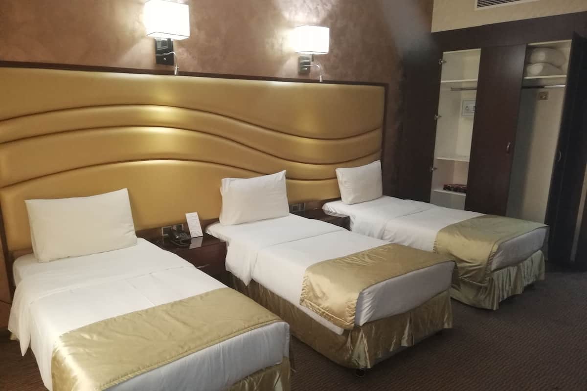 A hotel room with three single beds, each with a headboard and bedside tables.