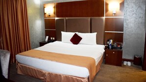 A hotel room with a large bed, a wooden headboard, bedside tables, a lamp, and a curtain. - Kings Park Hotel (Dubai)
