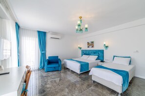 Una habitación de hotel con dos camas, un sillón azul, un escritorio y una araña.