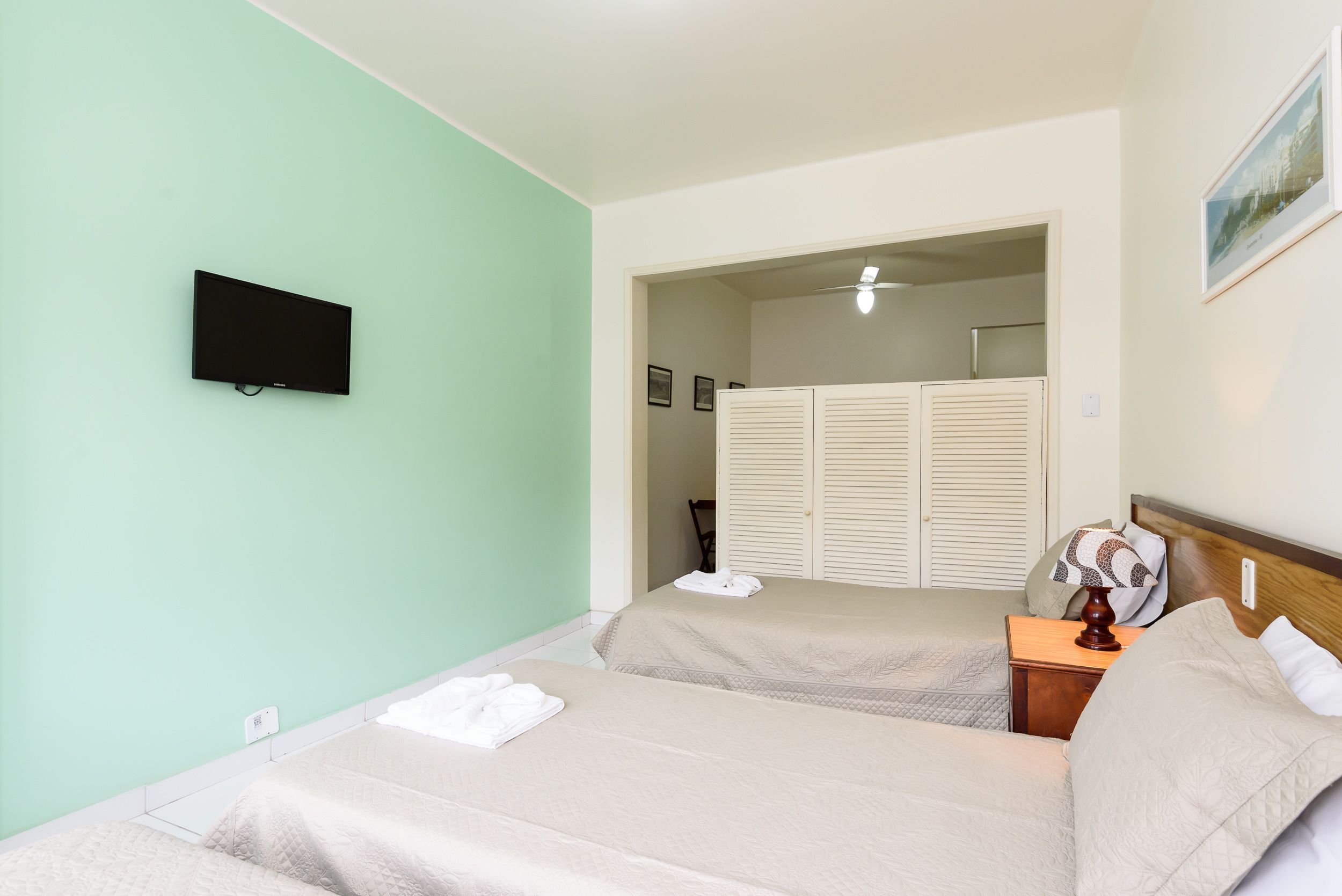 A hotel room with two beds, a TV mounted on the wall, a wooden nightstand, and a door leading to a bathroom.