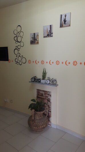 A living room with a fireplace, a wall-mounted shelf with decorative items, and a wall with circular and crescent designs. - Affittacamere da chris (Reggio Calabria)