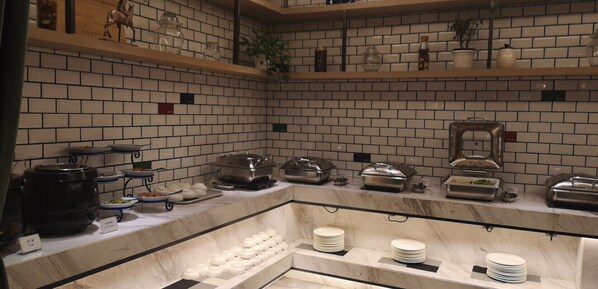 A buffet setup with various food items and serving utensils on a marble countertop.