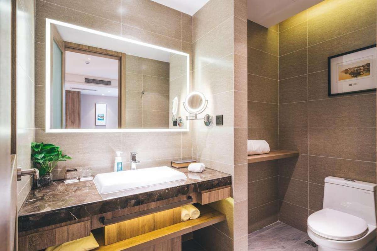 A modern bathroom with a marble sink, a large mirror with integrated lighting, a toilet, and a shelf with towels.