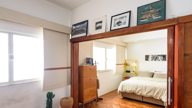 A bedroom with a wooden wardrobe, a bed with a white duvet, a small cactus plant, and a wooden floor. - Omar do Rio - BR902 (Rio de Janeiro)