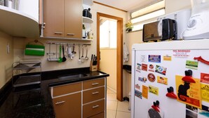 A compact kitchen with wooden cabinets, a black countertop, and a refrigerator covered with magnets. - Omar do Rio - BR902 (Rio de Janeiro)