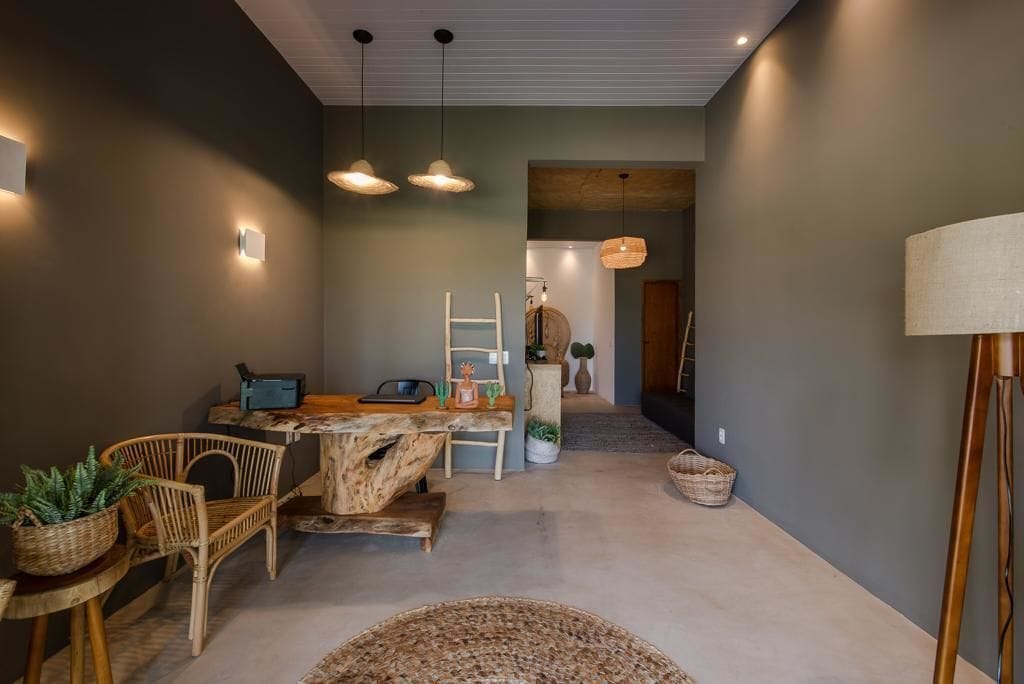 Um interior moderno com uma área de jantar, destacando uma mesa e cadeiras de madeira, um pequeno espaço de cozinha com escada e plantas, e um corredor que dá para outro cômodo.