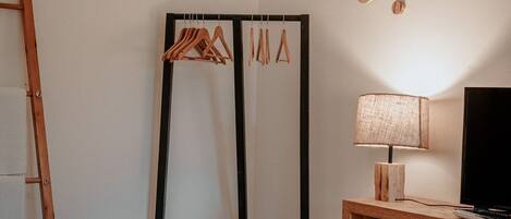 Een slaapkamer met een bed, een houten bureau, een televisie, een hanglamp en een kapstok met hangers.