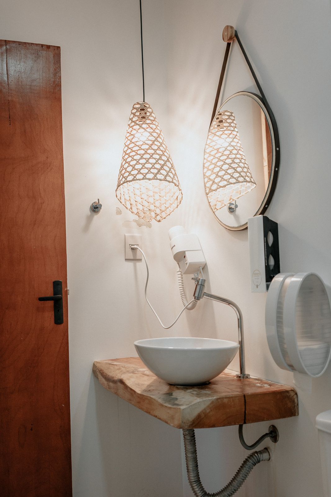 A bathroom with a wooden vanity, a white sink, and two pendant lights with a woven design.