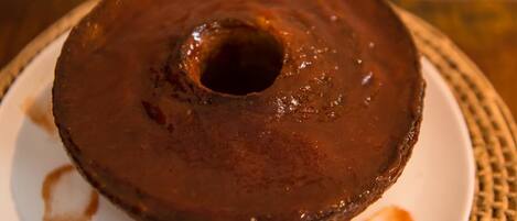 A chocolate bundt cake on a white plate with a patterned tablecloth.