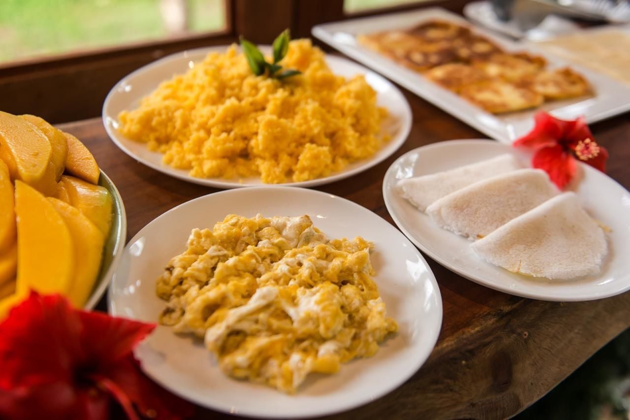 Una mesa con platos de huevos revueltos, puré de papas y un cuenco con mango en rodajas.