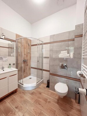 A modern bathroom with a glass-enclosed shower, a toilet, and a sink area.