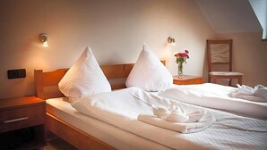 A hotel room with two beds, each with white linens and pillows, a nightstand with a lamp, and a small table with a vase of flowers.