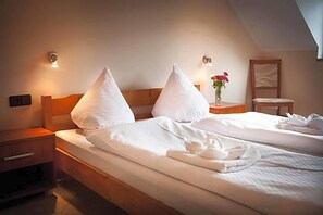 A hotel room with two beds, each with white linens and pillows, a nightstand with a lamp, and a small table with a vase of flowers.