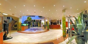 A spacious lobby with a central fountain, a reception desk, and a staircase.