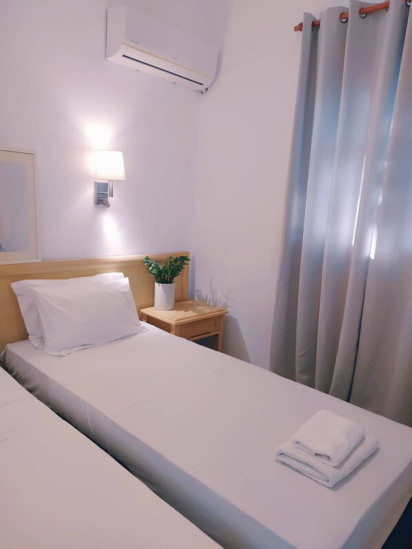 Ein Hotelzimmer mit einem Bett, einem Nachttisch mit Lampe, einer Topfpflanze und einem Fenster mit Vorhängen.