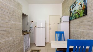 A compact kitchen with a refrigerator, a microwave, and a dining area with blue chairs. - Omar do Rio - PM408 (Rio de Janeiro)