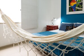 Una hamaca en un dormitorio con una cama, una mesita de noche, una lámpara y un cuadro en la pared.