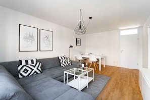 A modern living room with a grey sofa, a glass coffee table, and a dining area with a white table and chairs.