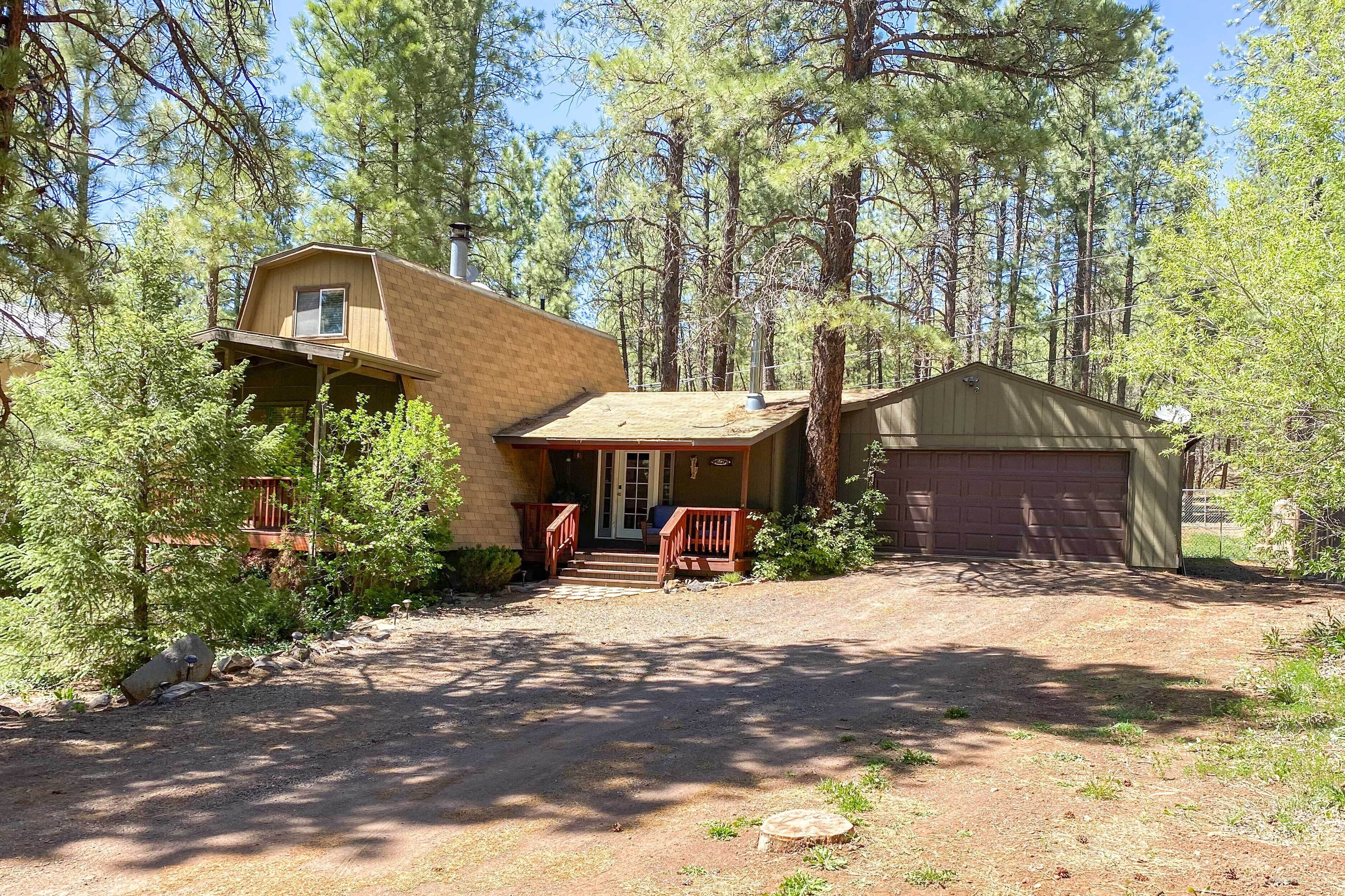 A two-story house with a front porch, a garage, and a wooded setting.