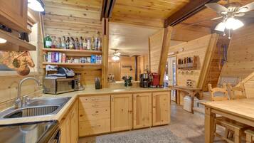 A wooden cabin interior with a kitchen area featuring a sink, cabinets, a microwave, and a coffee maker.