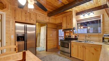 A wooden cabin kitchen with a refrigerator, stove, sink, and wooden cabinets.