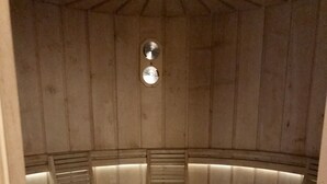 A wooden sauna with a circular design, featuring benches and a central heating element. - Hotel Piedibosco (Moena)