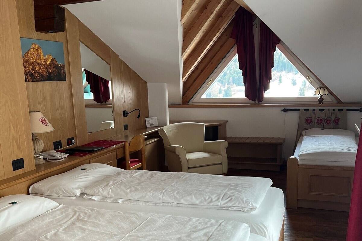 A bedroom with two beds, a desk, a chair, a mirror, and a window with curtains.