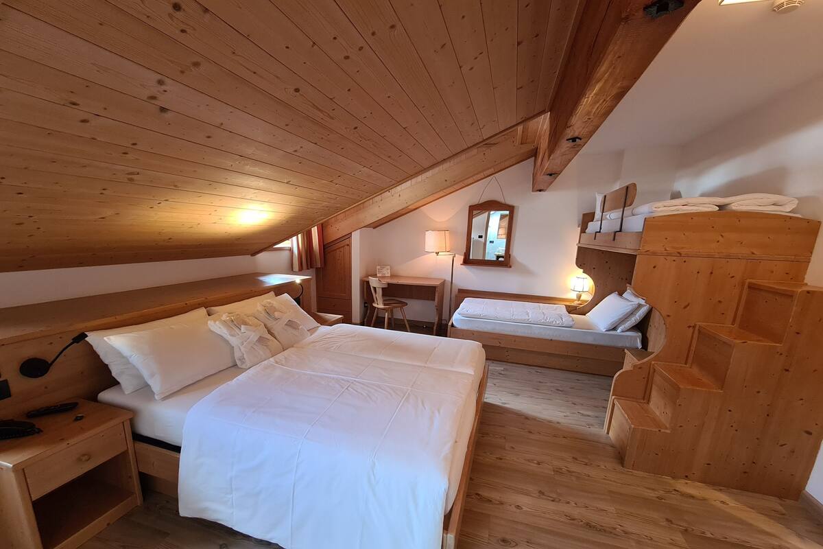 A cozy attic bedroom with two beds, wooden beams, a desk, and a mirror.