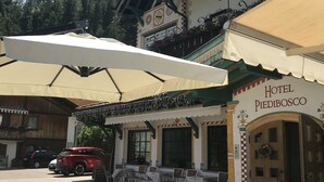 A hotel with outdoor seating, a clock, and a sign reading "Hotel Piedibosco". - Hotel Piedibosco (Moena)