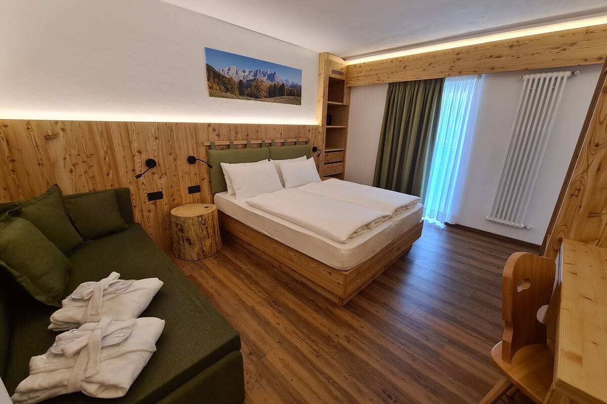 A wooden-paneled bedroom with a bed, a green sofa, and a wooden chair.