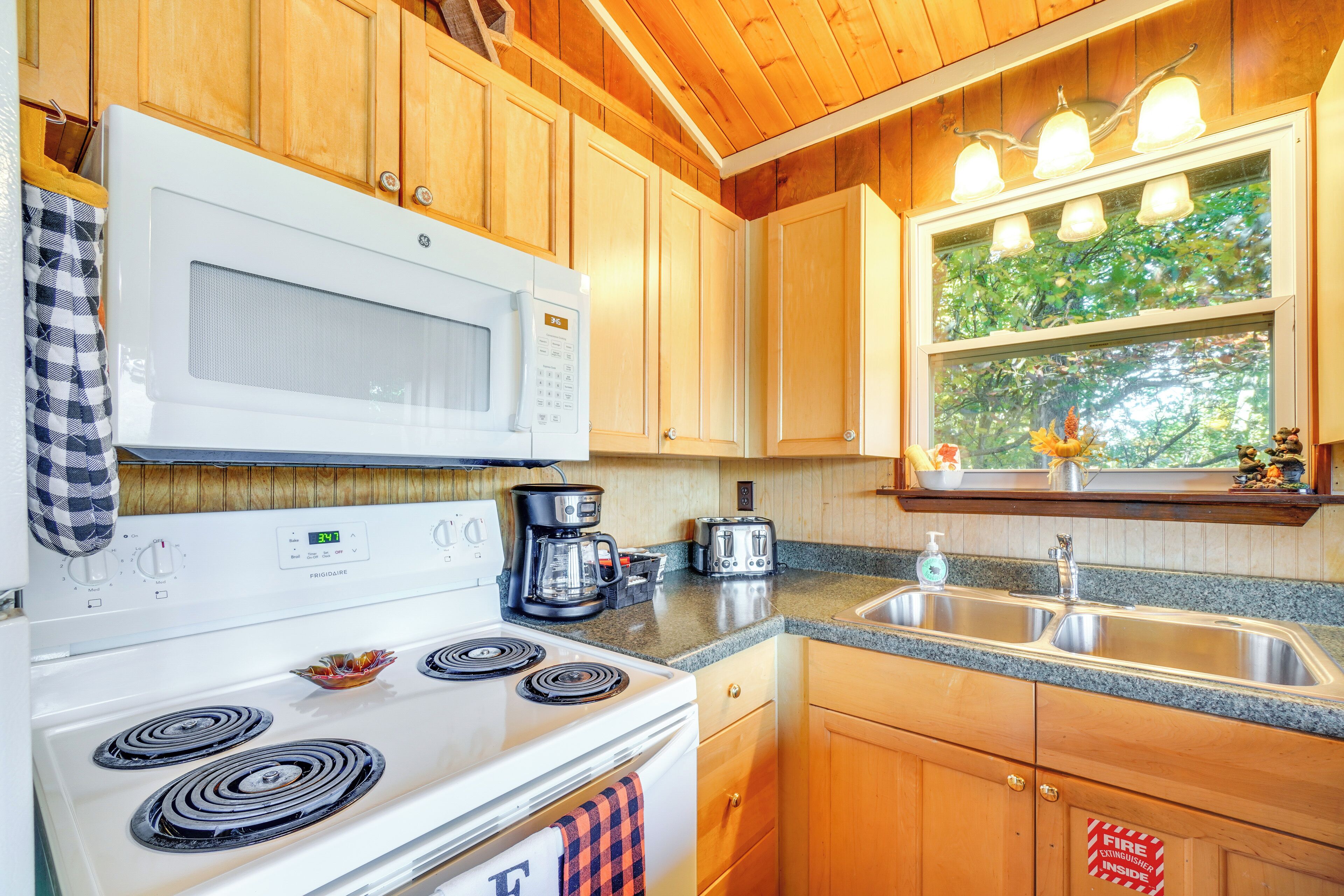 A kitchen with wooden cabinets, a white stove, a microwave, a coffee maker, and a sink.
