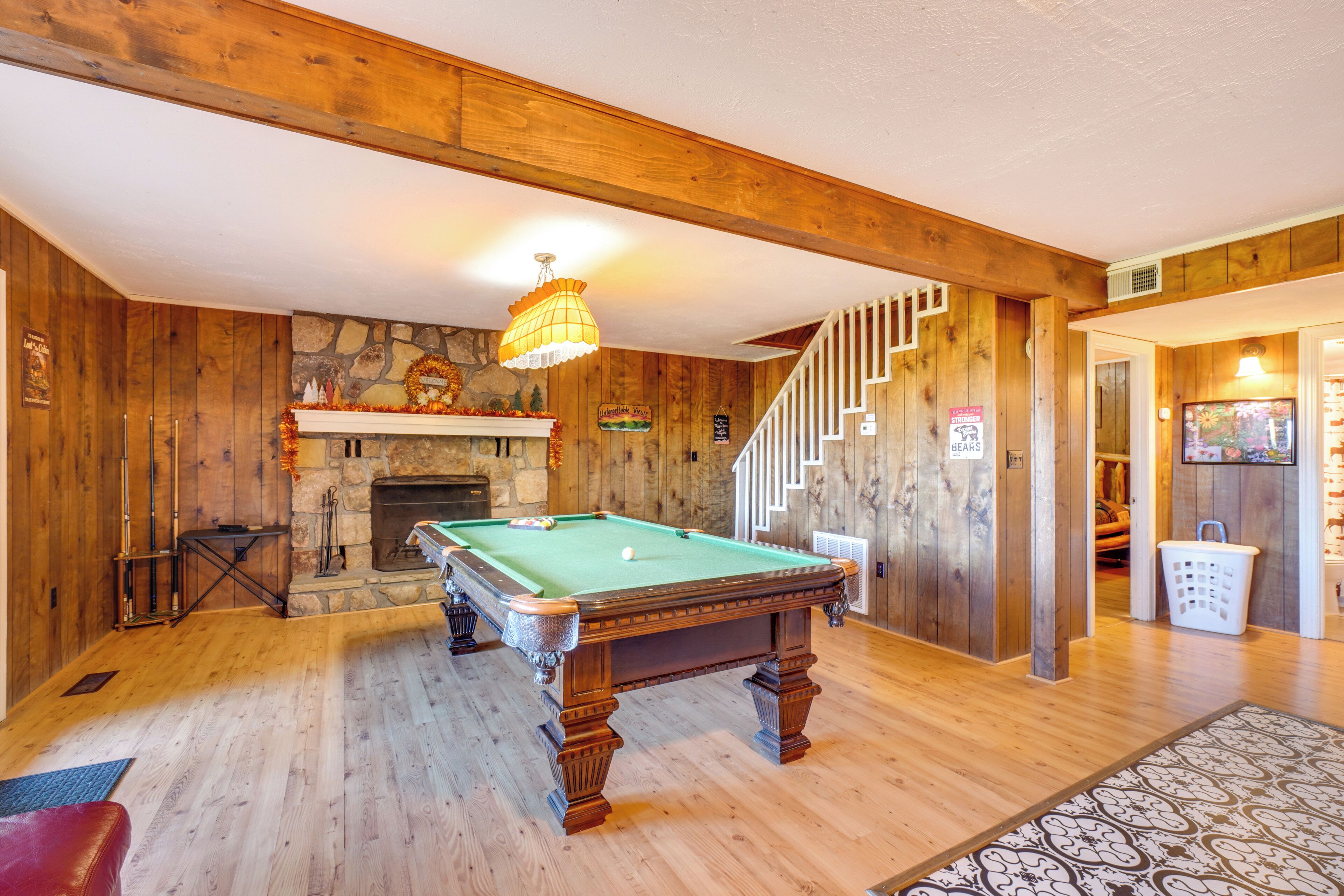 A pool table in a room with wooden walls and a stone fireplace.