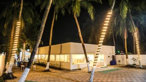 Un edificio moderno con fachada de vidrio, rodeado de palmeras e iluminado con luces colgantes.